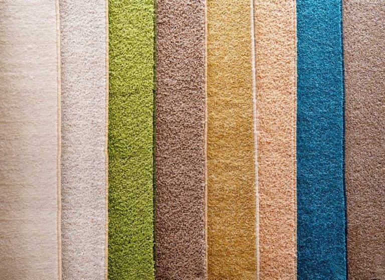 Variety Of Carpets And Carpets Of Different Colors On The Stand In The Store Or The Factory. Multicolored Carpet Samples